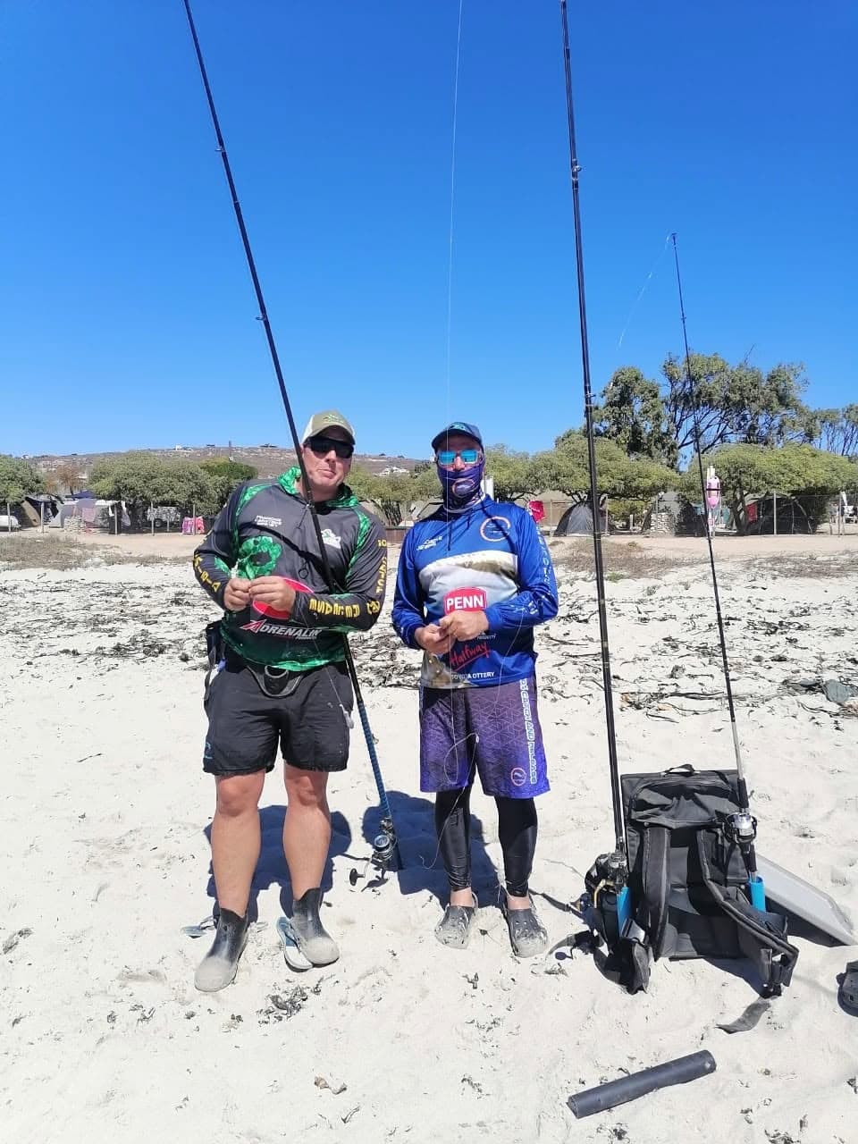 Two WP Bronzies members with fishing rods on the beach, with camp tents in the background