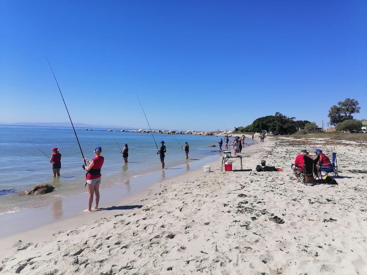Participants fishing along the shoreline at St Helena Bay, with camp seating set up on the beach
