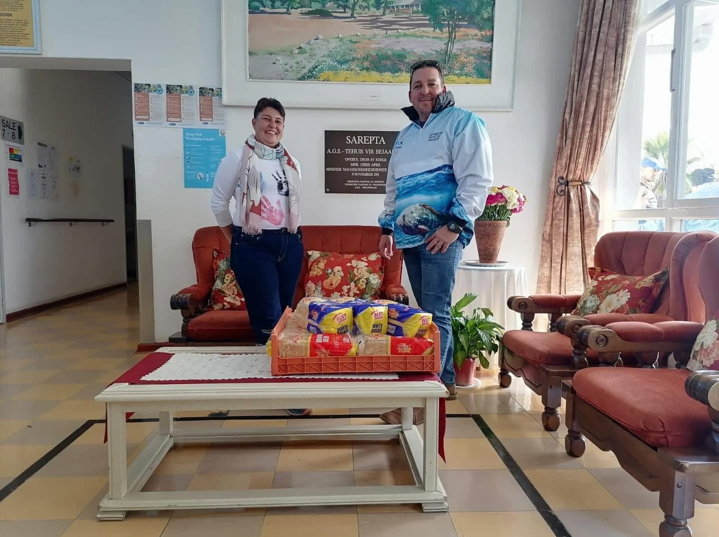 A WP Bronzies representative and a Sarepta representative with a crate of bread loaves in the Sarepta care home's lounge