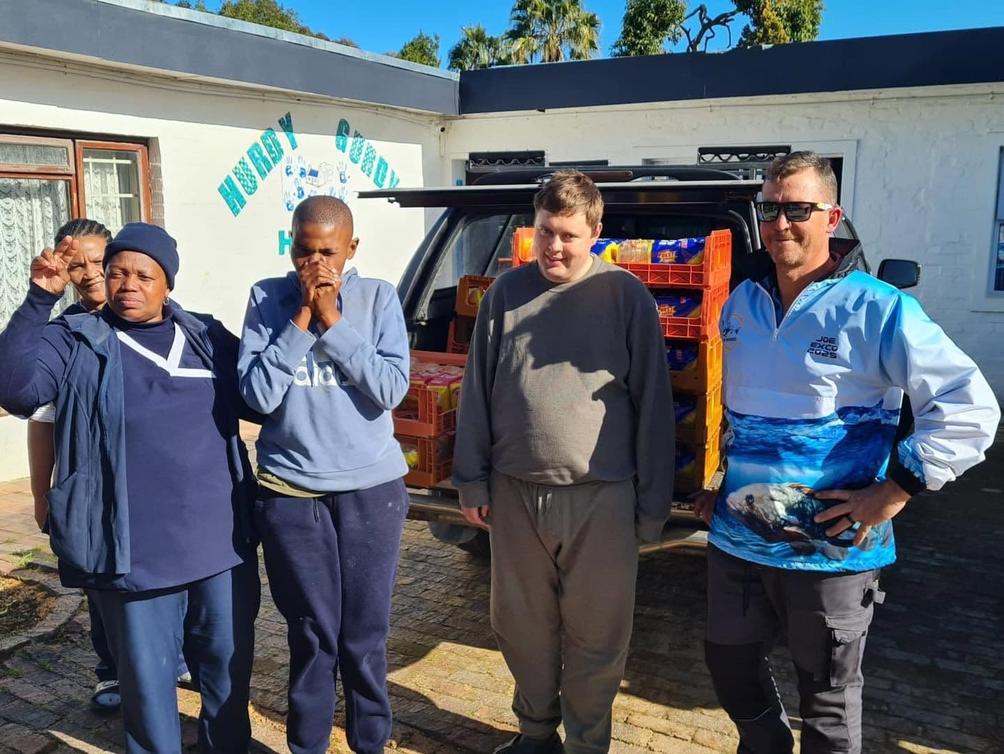 WP Bronzies representatives and Hurdy Gurdy House members outside the organisation's building, with a vehicle loaded with bread crates behind them
